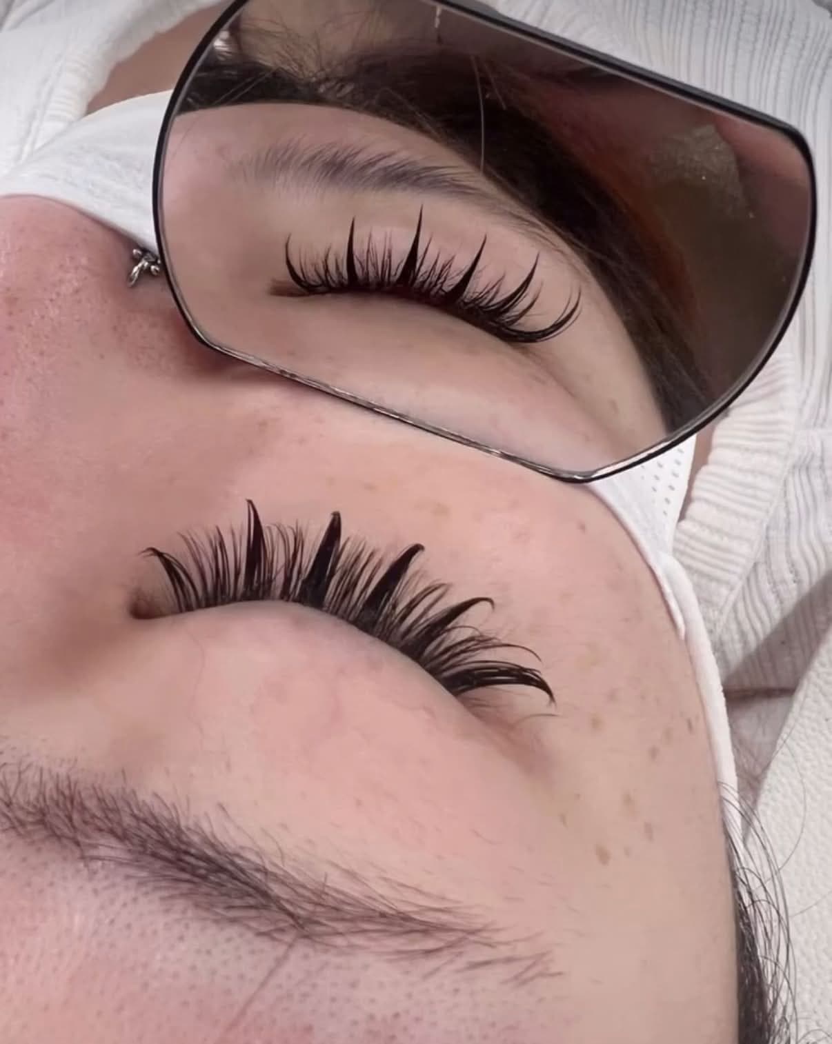 An anime lash set with bold spikes, seen on the closed eye and reflected in a hand mirror.